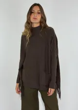 Sweater de punto color chocolate, con cuello alto, mangas largas y corte holgado. Presenta bolsillos delanteros y detalle de flecos en los laterales.