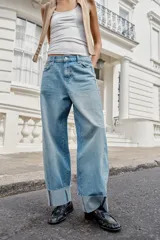 Jeans baggy de tiro medio con pernera holgada, diseño de cinco bolsillos y bajo acabado en vuelta. Cuenta con cintura elástica en la espalda y cierre frontal con cremallera y botón.