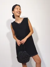 Vestido corto negro sin mangas, con escote a la base, confeccionado en tela texturizada y terminaciones con puntillas de estilo vintage.