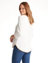 Remera de modal color blanco, con cuello redondo y mangas 3/4. Presenta un aplique bordado en color tostado en el cuello, los puños y el ruedo.