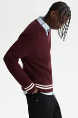Buzo de punto acanalado en color bordó, con cuello en V y detalles de rayas blancas en contraste en los puños y el ruedo. Presenta un corte boxy que ofrece una silueta amplia y estructurada.