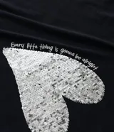 Remera de algodón color negro, con cuello redondo y mangas cortas. Presenta una estampa central en forma de corazón realizada con lentejuelas reversibles en tonos dorados y plateados.