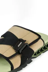 Sandalias tipo slide color beige con detalles en negro y suela verde.