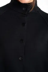 Cardigan negro de corte oversize, con cuello alto, cierre frontal de botones y mangas tres cuartos. Presenta un diseño holgado con bolsillos frontales y una caída fluida.
