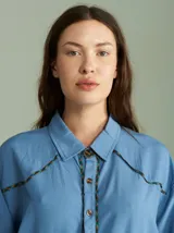 Camisa celeste de algodón, de corte básico y caída suelta, con detalles de vivos en cuadrillé en la botonera y los hombros.