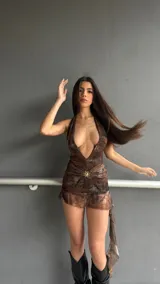 Vestido corto marrón con estampado abstracto, escote halter profundo y detalle de broche dorado en el centro del busto. La falda es corta y con volados. Incluye un short.