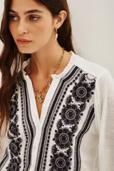 Camisa de algodón y viscosa color blanco, con mangas largas y diseño frontal con bordados geométricos y florales en contraste negro. Presenta cuello redondo con pequeña abertura y cierre frontal de botones.