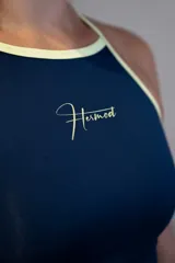 Musculosa deportiva de lycra color azul marino con ribetes y tirantes finos en color amarillo claro. Presenta un logo caligráfico en color amarillo claro en el pecho.