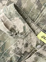 Pantalón de tiro alto, corte recto y amplio, confeccionado en sarga resistente con un estampado all-over camuflado en tonos verde militar y beige, con líneas verticales de pespuntes claros. Cuenta con cierre de cremallera y bolsillos delanteros y traseros.