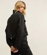 Campera corta de jean color negro con cuello inglés, abotonadura frontal, bolsillos tipo parche con solapa en el pecho y mangas largas.