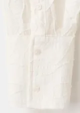 Blusa de diseño recto color crudo con diseño bordado floral, cuello camisero, manga larga con puños anchos abotonados y cierre delantero con botones.