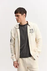 Campera con cierre frontal y capucha, confeccionada en tejido de algodón texturado color off-white, con bolsillos delanteros y detalles estampados en el pecho.