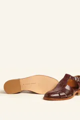 Sandalia cerrada tipo pescador de cuero negro charol, con tira en T y hebilla ajustable en el tobillo. Posee suela y taco bajo de madera.