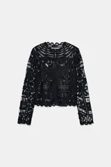 Blusa negra de manga larga confeccionada en tejido tipo crochet con intrincados patrones geométricos y florales. Presenta cuello redondo y cierre frontal con botones.