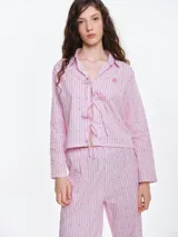 Camisa de dormir de popelina de algodón, con estampado de rayas verticales y pequeños motivos geométricos. Presenta cuello camisero, mangas largas y cierre frontal mediante lazos ajustables.