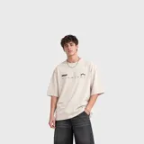 Remera beige de algodón con calce oversize y cuello redondo. Presenta un pequeño estampado frontal en el pecho con texto y tres estrellas negras.