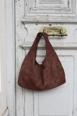 Cartera tipo hobo de gamuza color marrón, con diseño minimalista y asa integrada.