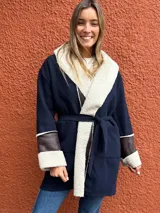 Saco de paño azul marino con solapas amplias y puños en corderito sintético color crema. Presenta detalles en cuero sintético marrón en la parte frontal y en las mangas, con un diseño abierto y corte recto.
