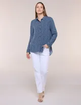 Camisa de rayón azul marino con estampado de lunares pequeños en tonos claros, cuello camisero, cierre frontal de botones, mangas largas y ruedo curvo asimétrico más largo en la espalda.