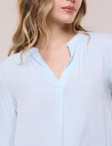 Blusa celeste fluida de viscosa, con escote en V y cuello mao, mangas largas y pliegue central en el delantero.