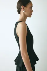 Top sin mangas con escote bote, costuras moldeadoras y pliegues en la cintura que forman un peplum acampanado. Cuenta con cierre oculto en la espalda y diseño de corte sastre en color negro.