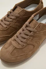 Zapatillas de estilo urbano color chocolate, confeccionadas en material textil tipo gamuza, con cordones al tono y suela de goma plana.