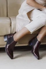 Botín chelsea de cuero vacuno color bordó con acabado charol, punta fina y elástico lateral negro. Posee un taco ancho y bajo de goma.