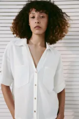 Camisa crop de mezcla de lino color blanco, con cuello solapa, escote en V, manga corta con trabilla, bolsillos de plastrón en el delantero y cierre frontal de botones.
