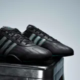 Championes Adidas Adiracer de perfil bajo inspirados en el automovilismo, en color negro con detalles plateados y turquesa. Presentan diseño de tres tiras en los laterales, empeine de cuero con inserciones sintéticas y suela de goma.