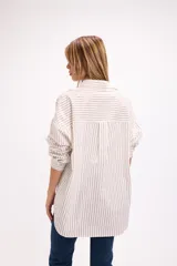 Camisa de corte oversize con estampado de rayas verticales finas en color azul sobre fondo claro. Presenta cuello clásico, cierre frontal con botones y un bolsillo aplicado en el pecho.