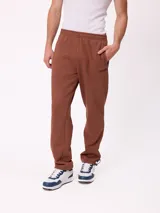 Pantalón tipo babucha de algodón y poliéster en color marrón, con cintura elástica, bolsillos laterales y logo de la marca bordado en la pierna izquierda.