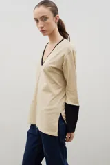 Remera de algodón con escote en V, manga larga y diseño bicolor. Presenta cuerpo en color beige con detalles en negro en el escote, los puños y los tajos laterales.