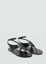 Sandalias planas de cuero color negro, estilo thong, con tira ajustable al tobillo mediante hebilla metálica dorada y punta redonda.