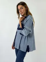 Saco de punto color naranja con detalles de rayas horizontales en las mangas y franjas verticales en el cuerpo. Tiene cuello tipo polo, cierre frontal con botones y un bolsillo decorativo en el pecho.