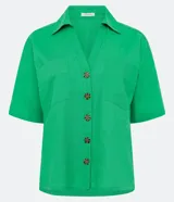 Camisa de manga corta confeccionada en mezcla de viscosa y lino color turquesa. Presenta cuello camisero con escote en V, bolsillos frontales de parche y cierre frontal con botones geométricos de efecto carey.