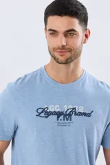 Remera de manga corta color celeste melange, con cuello redondo y diseño clásico. En el frente presenta una combinación de estampa y bordado en tonos azul marino y blanco con la inscripción 'Legacy Brand'.
