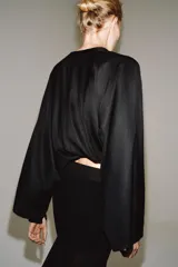 Camisa negra de cuello redondo y manga larga ancha con silueta fluida, con cierre frontal de botones y aberturas laterales en el bajo.
