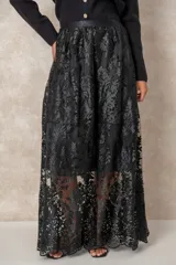 Pollera larga de encaje negro con diseño floral bordado, que presenta una capa superior transparente y un forro interno corto a tono. Posee una cintura alta con pretina lisa.