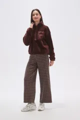 Buzo de polar tipo peluche color chocolate, con cuello alto y cierre frontal parcial. Presenta un bolsillo frontal con cierre y detalle de tela técnica en contraste.