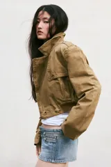 Trench corto de cuello solapa y manga larga, con diseño cruzado y cierre frontal con botones. Presenta bajo acabado en elástico y trabillas en los hombros.