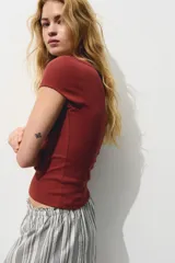 Top corto ajustado de punto acanalado color terracota, con mangas cortas y escote bote con detalle de solapa en los hombros.