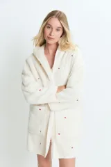 Saco de textura tipo peluche, color crema, con capucha y bolsillos frontales. Presenta un estampado sutil de corazones rojos dispersos por toda la prenda.