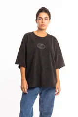 Remera de corte boxy fit, color negro con efecto lavado, de manga corta y cuello redondo. Presenta un logo bordado en el centro del pecho dentro de un óvalo.