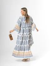 Maxi vestido largo de fibrana en color blanco con estampado paisley y geométrico en tonos azules y tostados, con escote en V, mangas largas amplias y diseño holgado con volados en la falda.