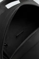 Mochila negra con textura y acabado engomado. Tiene un compartimento principal con cierre de cremallera, un bolsillo interior con cierre, un bolsillo frontal con cierre, un asa de mano, dos asas de hombro ajustables, parte posterior acolchada y banda de sujeción para equipaje.