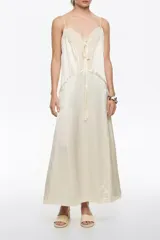 Vestido midi color crema o blanco roto, con tirantes finos y escote en pico adornado con encaje. Presenta paneles de tejido con textura arrugada y un lazo decorativo en el centro del escote.