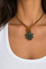 Collar de diseño artesanal con cordón de cuero tostado y dije de cerámica verde en forma de flor.