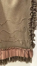 Ruana de tejido con textura en color bordó, con diseño amplio y fluido. Presenta detalles de volados aplicados en el cuello y ruedo, terminaciones con flecos y lazo frontal regulable.