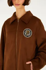 Campera de calce relajado color marrón, con cuello amplio, cierre frontal y mangas largas, confeccionada en tejido de acabado gamuzado con un parche bordado en el pecho.