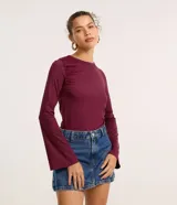 Blusa de manga larga color vino tinto, confeccionada en microfibra, con cuello redondo y fruncido en la zona del pecho y hombros. Las mangas terminan en un corte acampanado (tipo godê).
